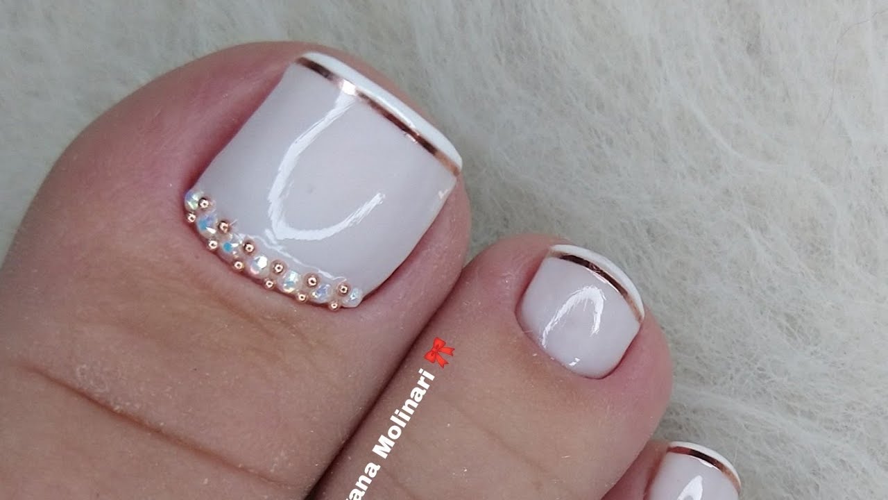 Unhas dos pés esmaltadas em branco com detalhes dourados